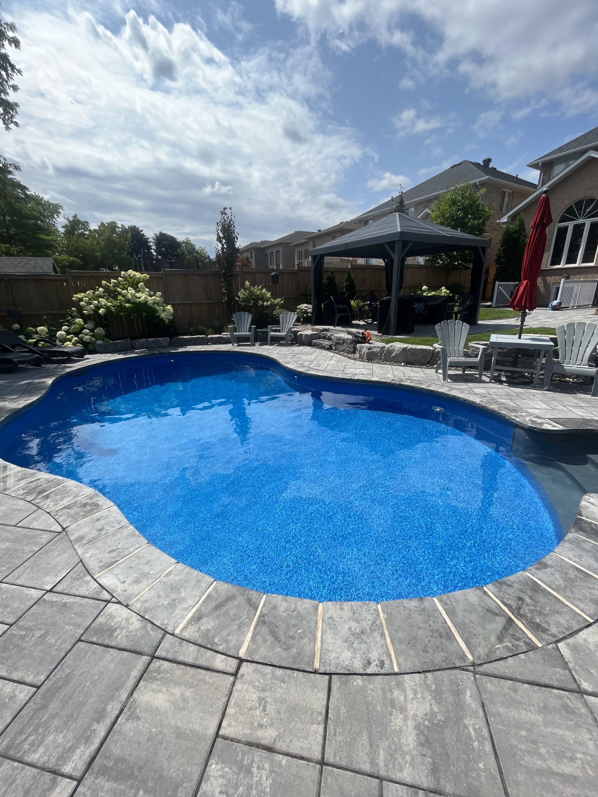 Elegant kidney-shaped pool featuring natural stone coping integrated into backyard landscaping in Ajax